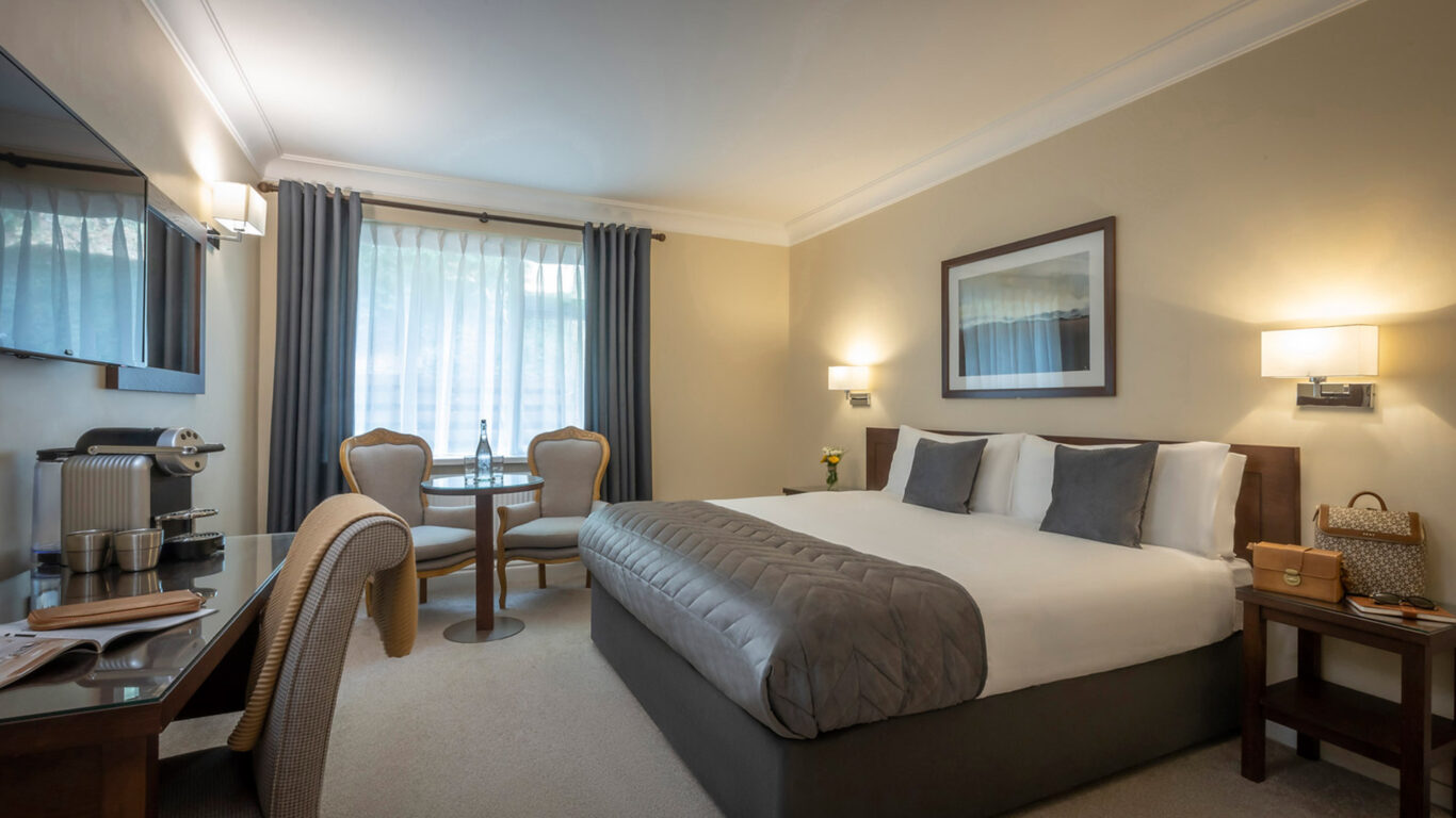 Elegant hotel room with king-size bed, plush seating, large window, and modern amenities like coffee maker and flat-screen TV.