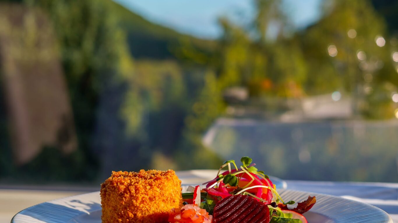 Delicious gourmet salad and crumbed cake served on a patio with stunning mountain views, perfect for a relaxing dining experience.
