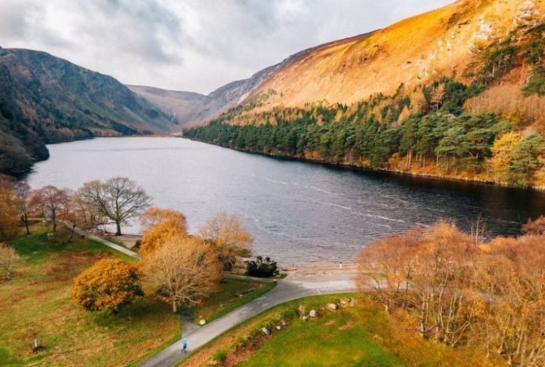 Scenic lake with vibrant autumn trees, mountain views, and a winding path inviting peaceful strolls.