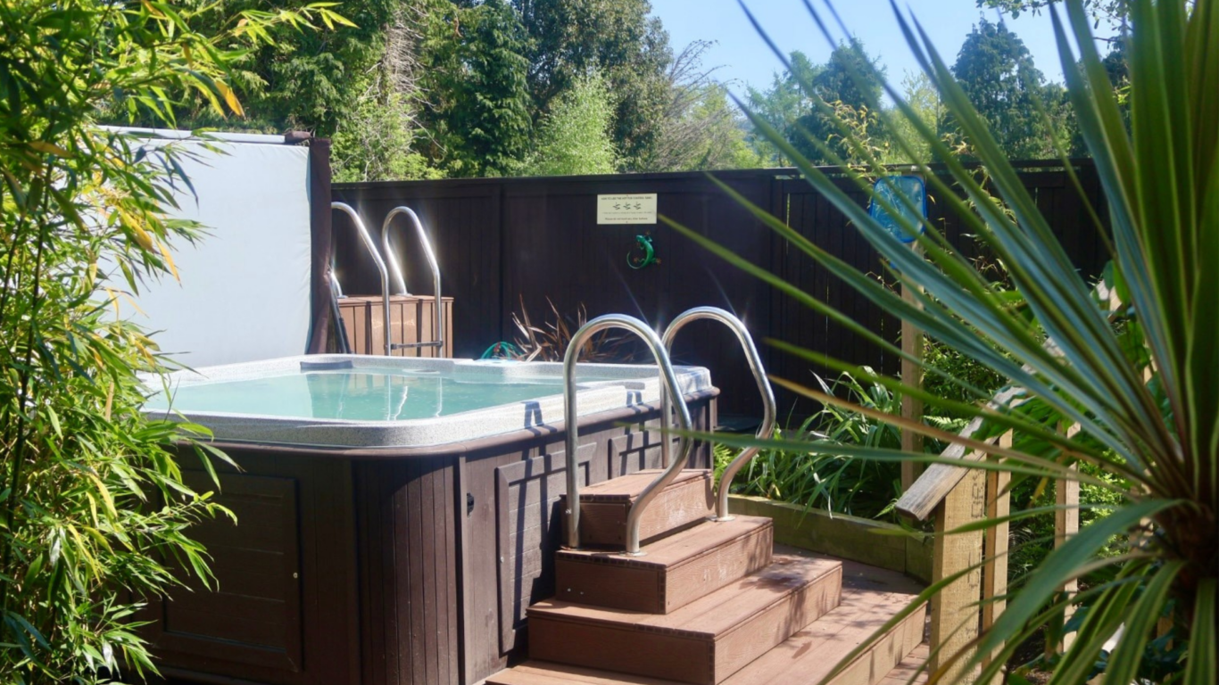 Relax in our serene garden hot tub surrounded by lush greenery, unwind under the clear blue sky, and enjoy peace and privacy.