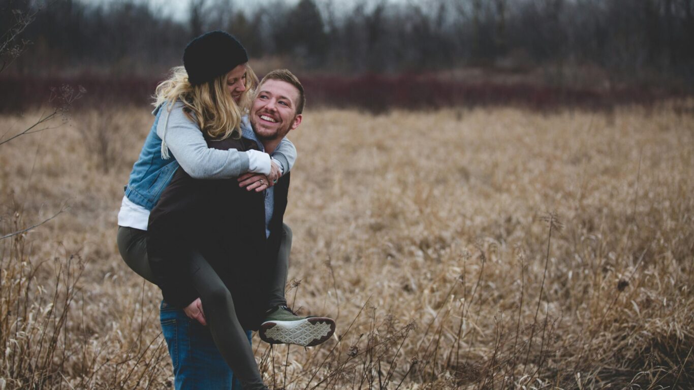 Couple enjoying a cosy moment in a picturesque grassy field, perfect for romantic hotel getaways and nature escapes.