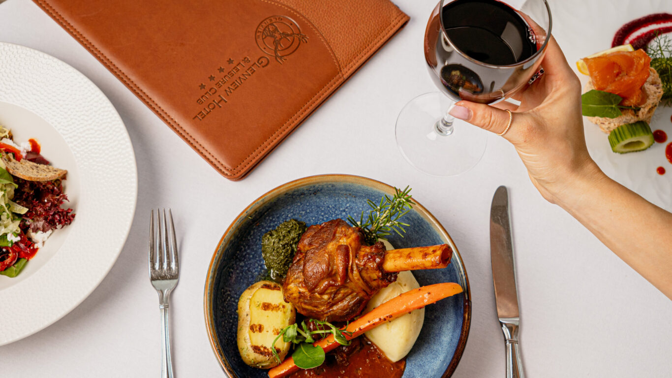 Elegant hotel dining with gourmet lamb shank, fresh salad, smoked salmon, fine wine, and leather menu in cosy restaurant.