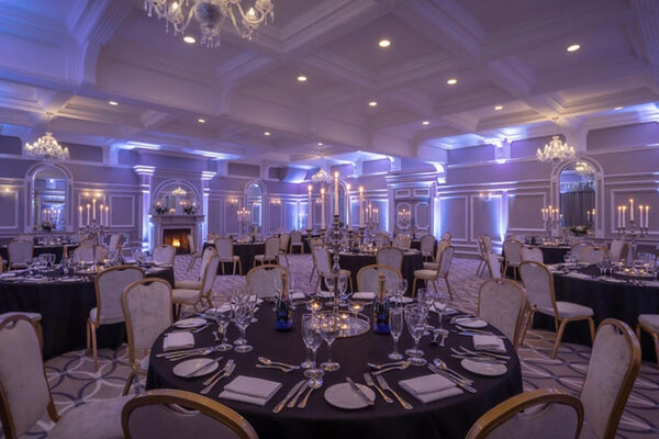 Elegant hotel banquet hall with chandeliers, soft lighting, round tables set with fine dining ware, perfect for events.