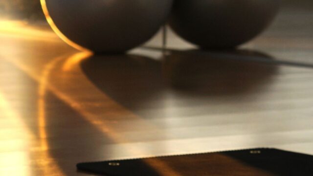 Sunlit hotel gym with yoga mat, dumbbells, and exercise balls on hardwood floor, inviting fitness and relaxation.