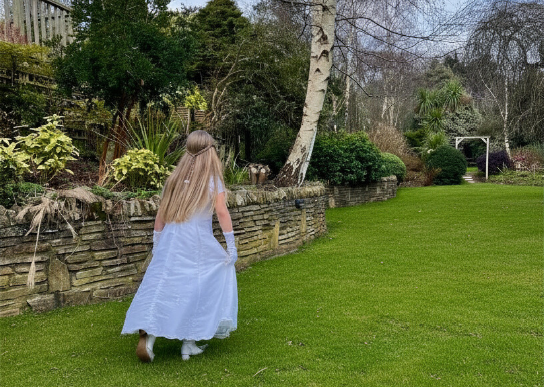 Child in white dress wanders a lush garden with stone walls and trees, creating a serene, family-friendly hotel experience.