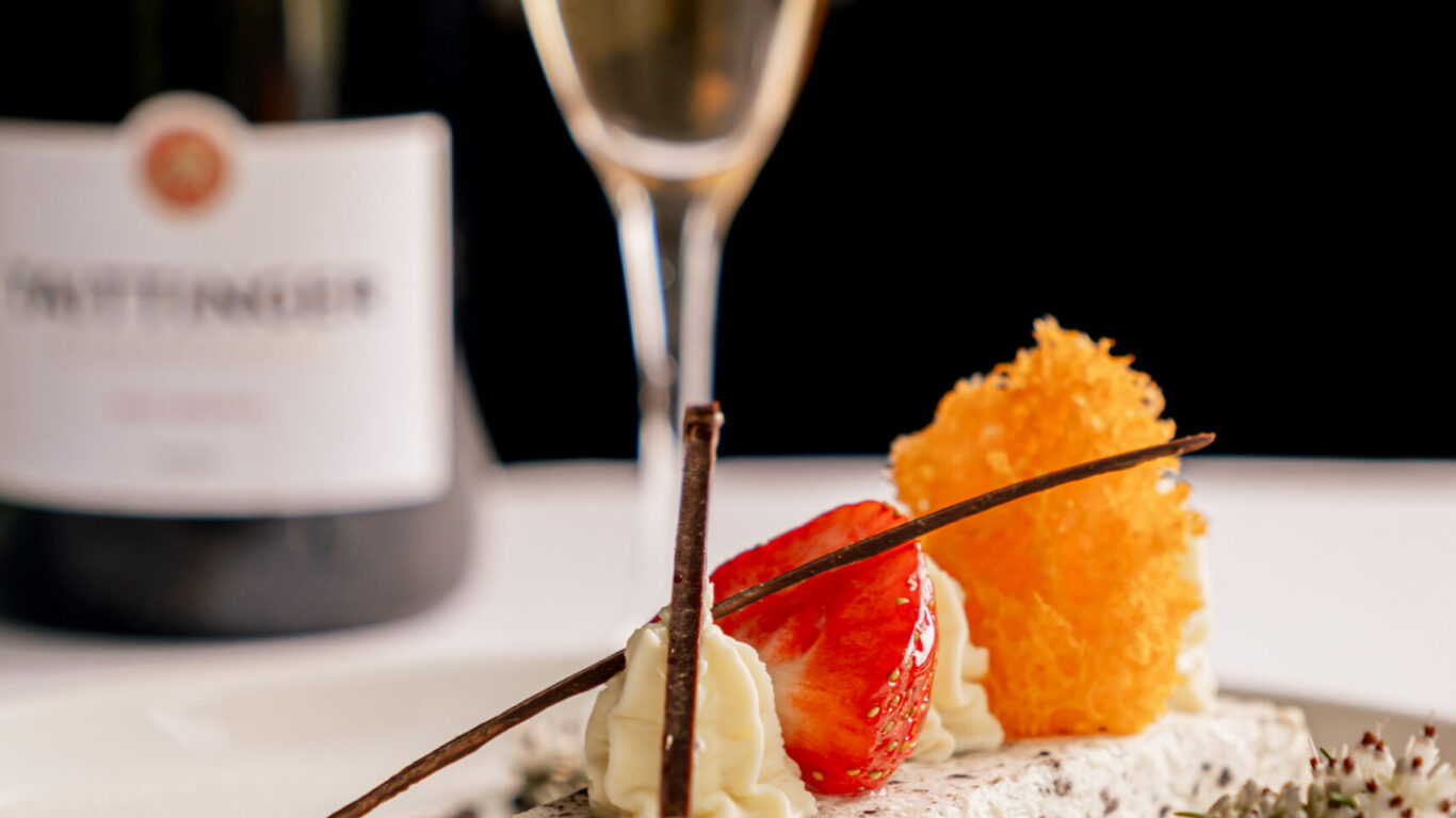 Indulge in a creamy dessert with fresh strawberries, paired with sparkling wine, at our luxury hotel's elegant dining.